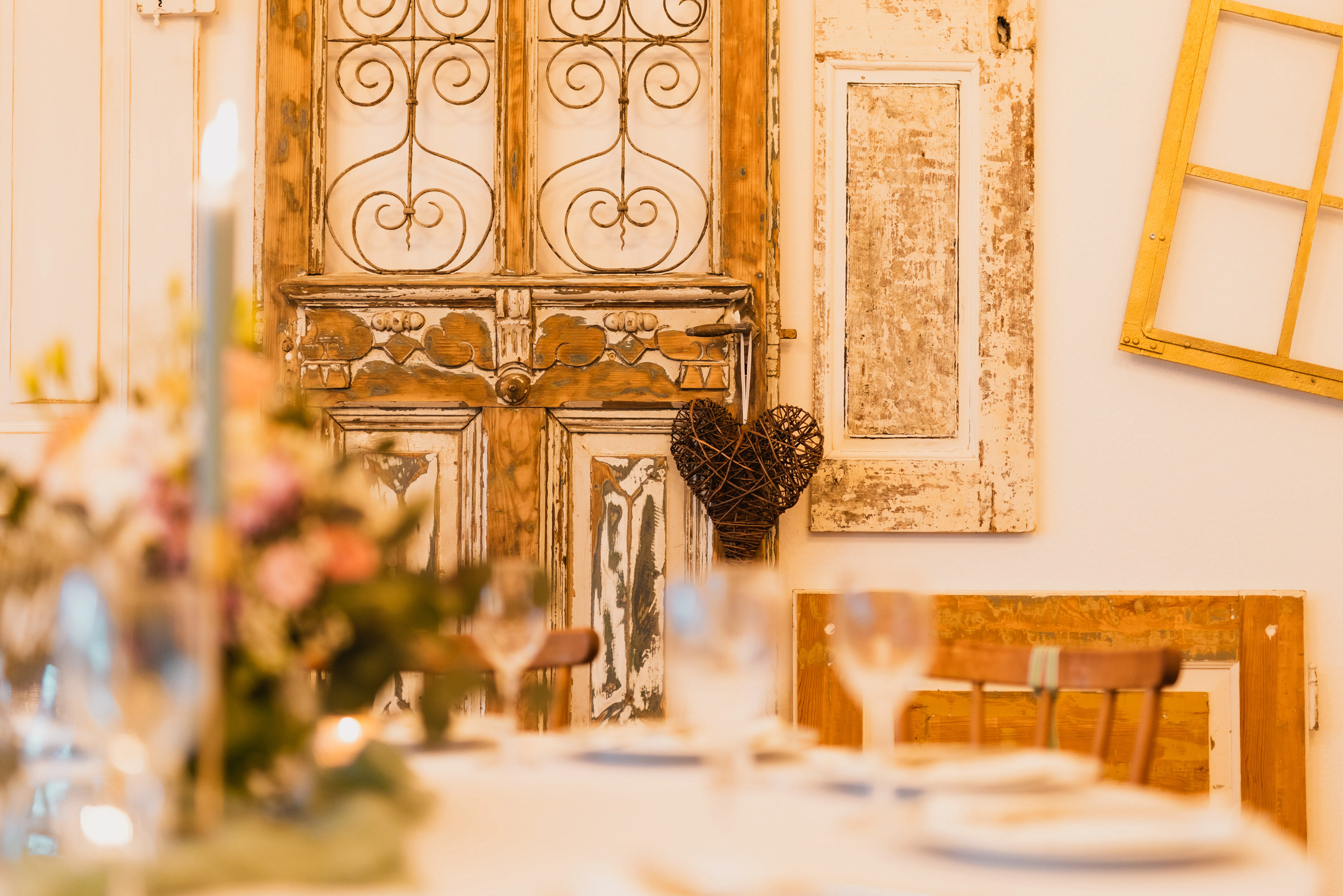 Antike Tür mit Eisenornamenten als Wanddeko im Festsaal, davor unscharf ein gedeckter Tisch mit Blumen
