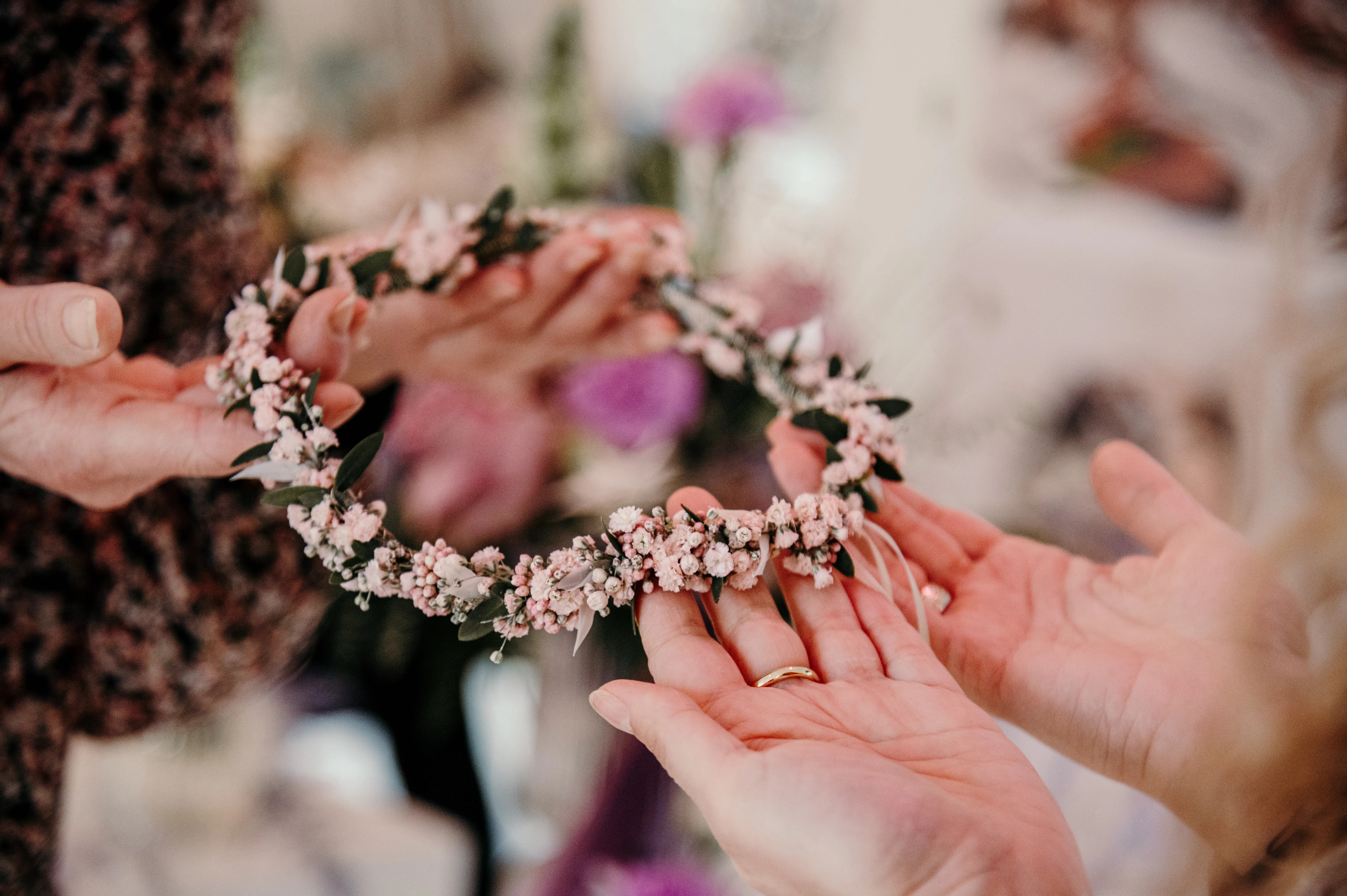 Hände halten einen zarten Blumenkranz aus rosa Trockenblumen und grünen Blättern