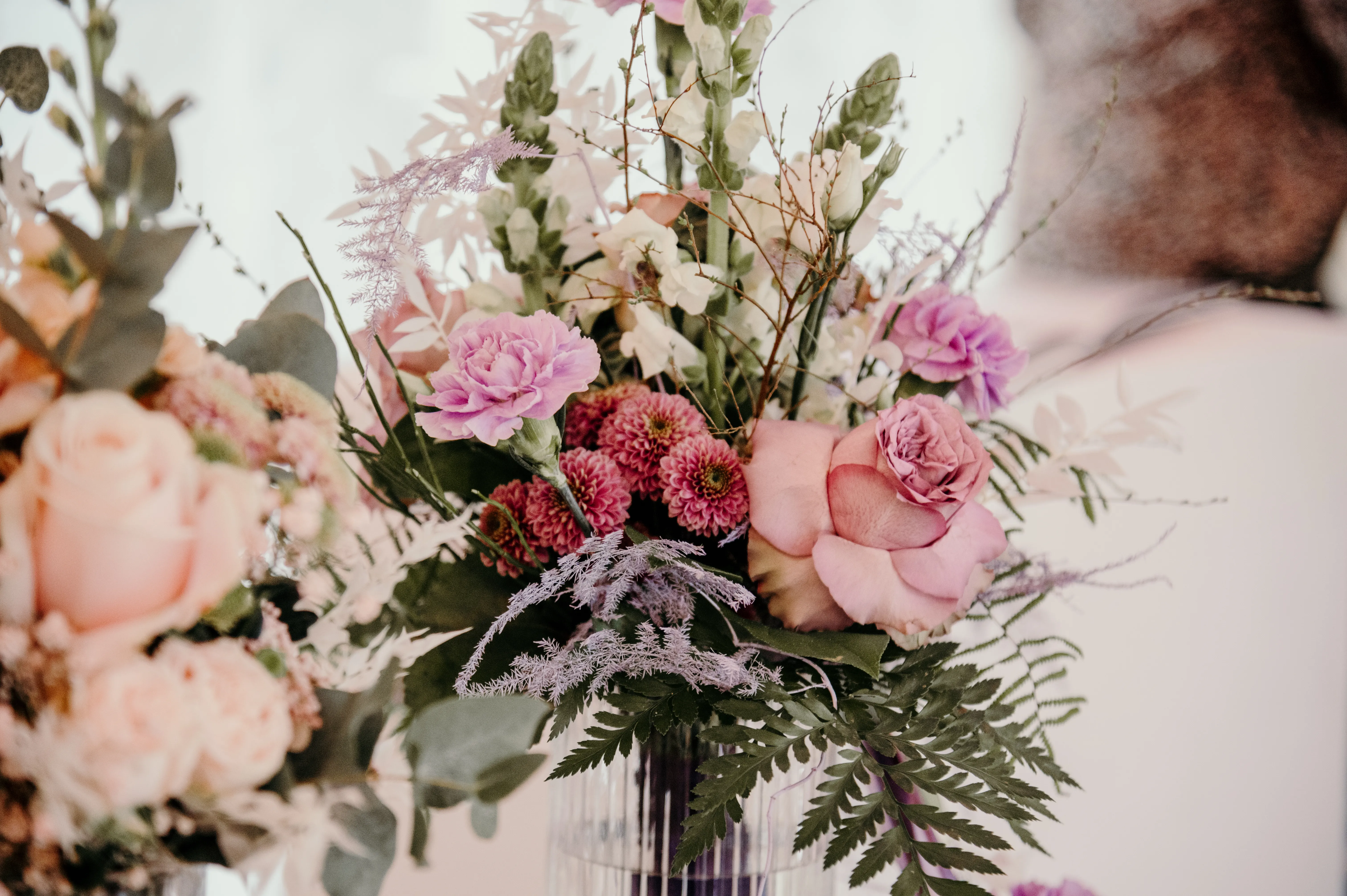 Üppiger Blumenstrauß in Rosa und Flieder mit Rosen, Nelken und Farn in einer Glasvase