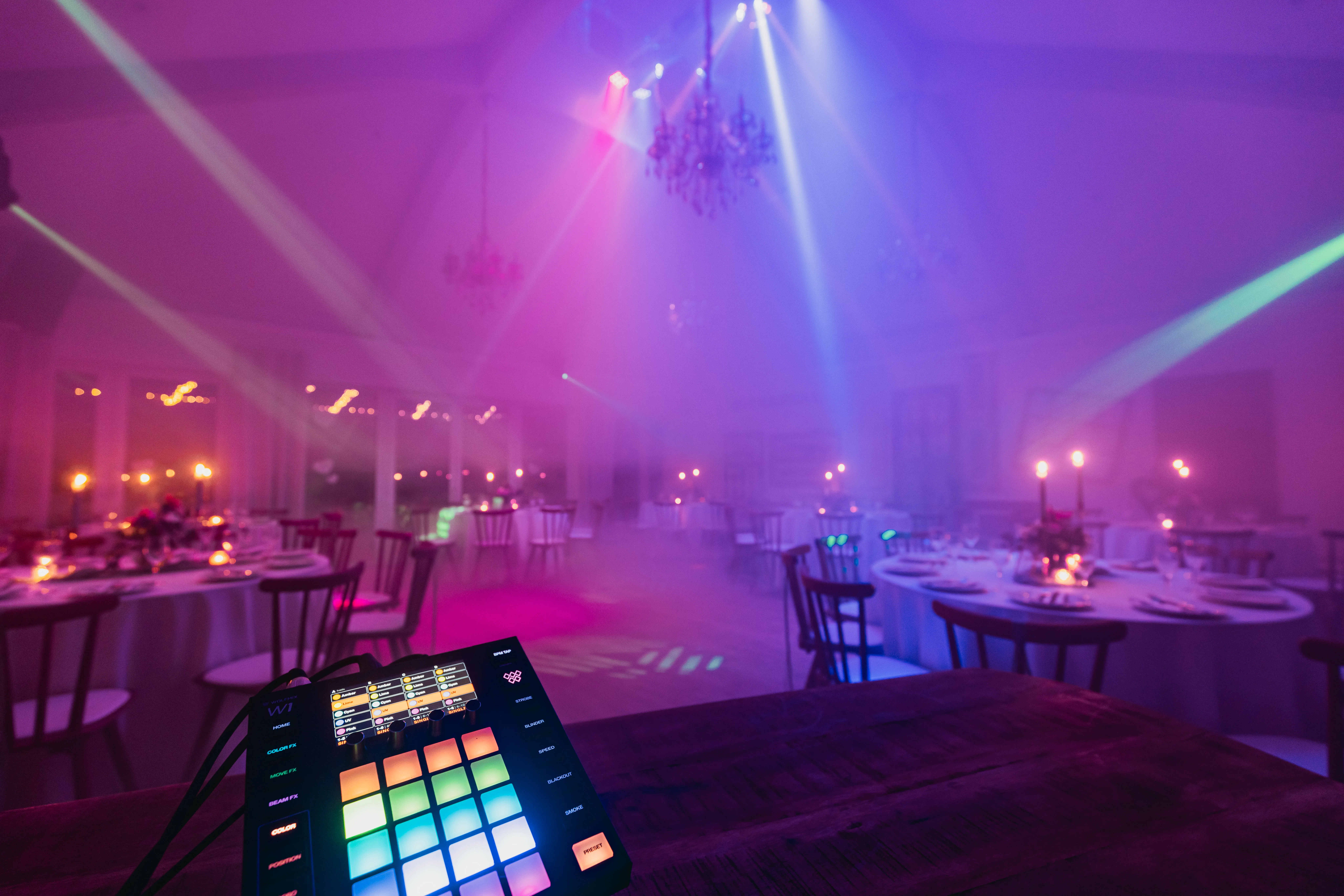 DJ-Controller mit bunten Pads im Vordergrund, dahinter der Festsaal mit Lichtshow und gedeckten Tischen