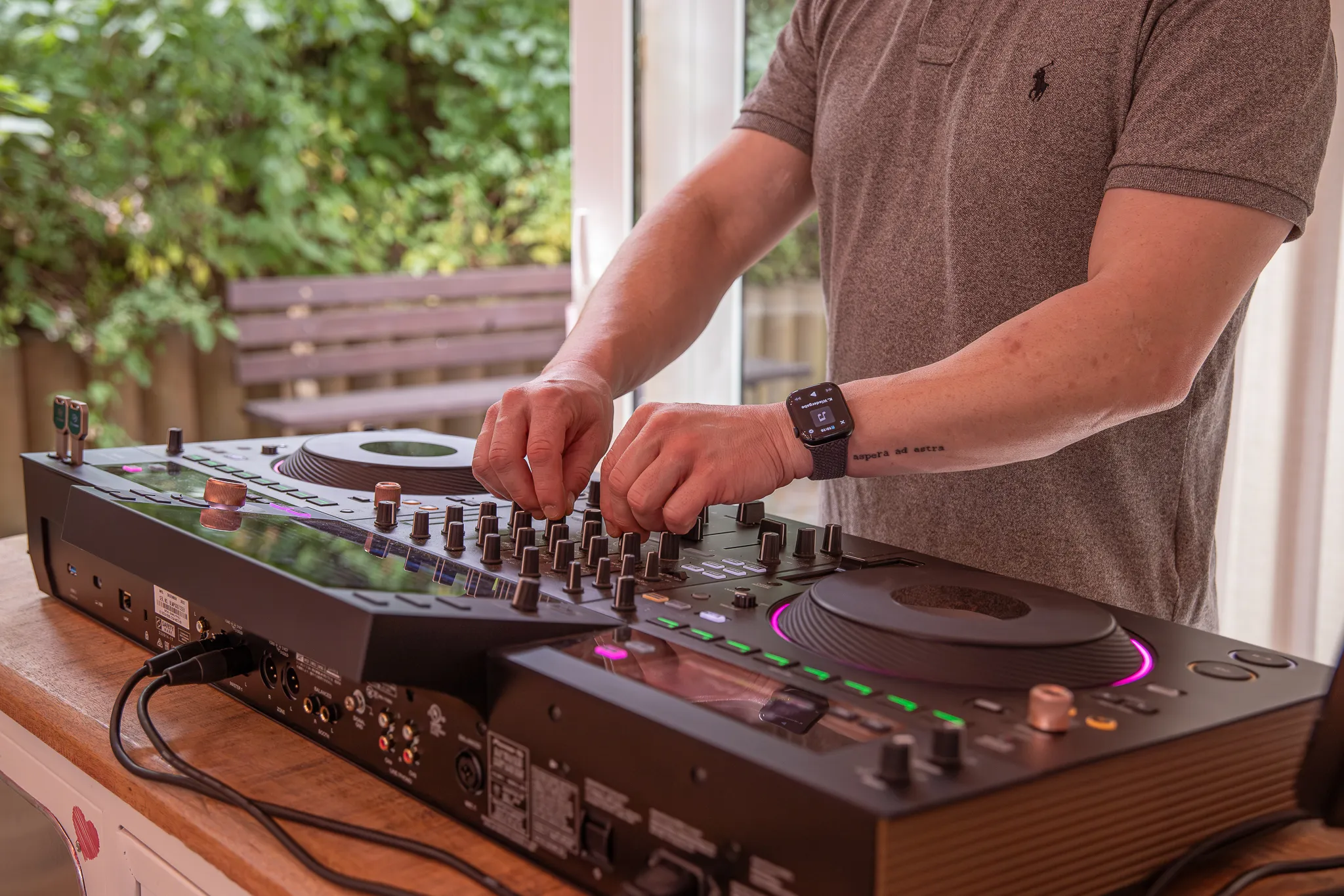 DJ bedient Mischpult mit Jogwheels vor geöffneter Terrassentür bei Tageslicht
