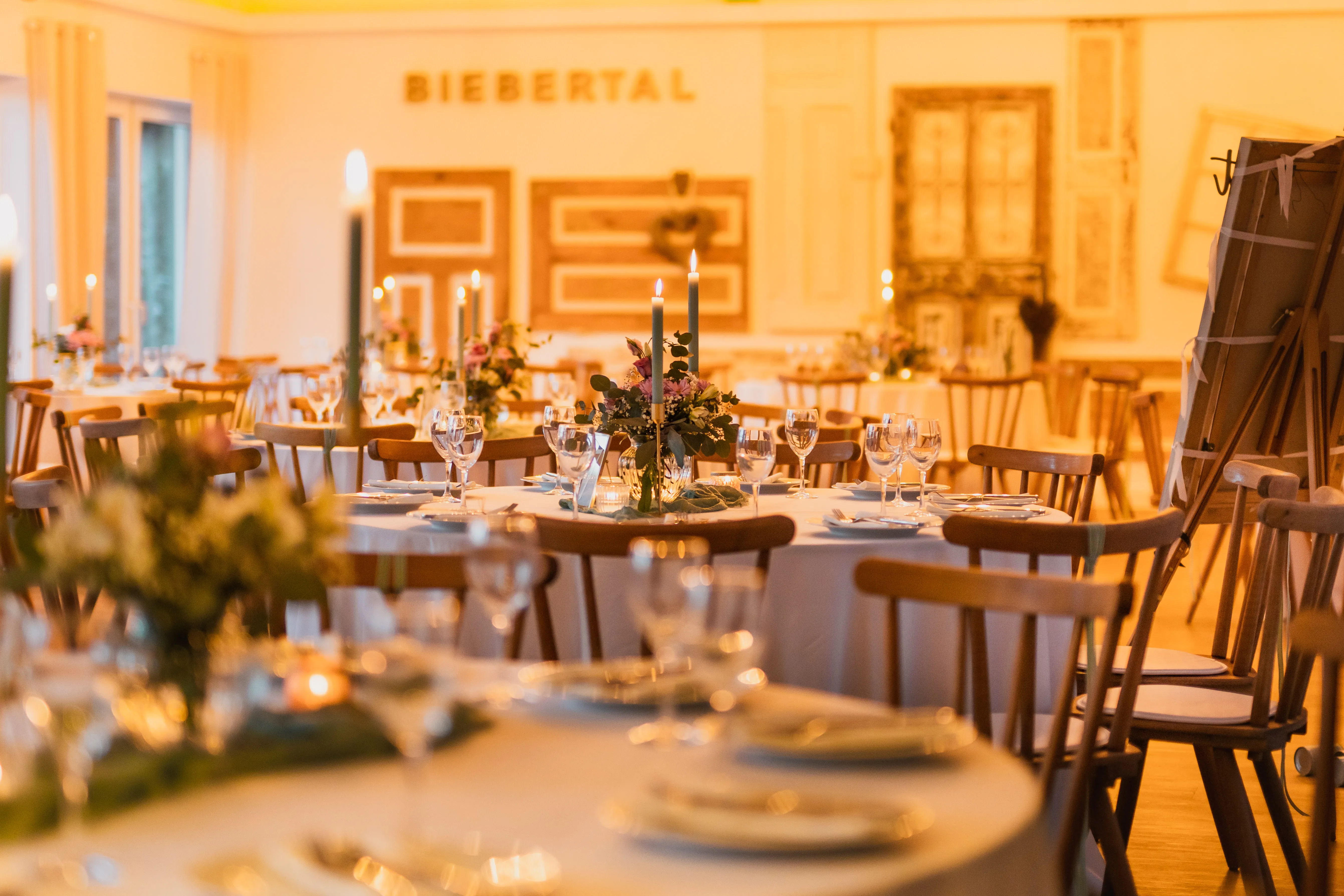 Runde Hochzeitstische mit Kerzen und Blumen im warm beleuchteten Festsaal des Hotel Biebertal