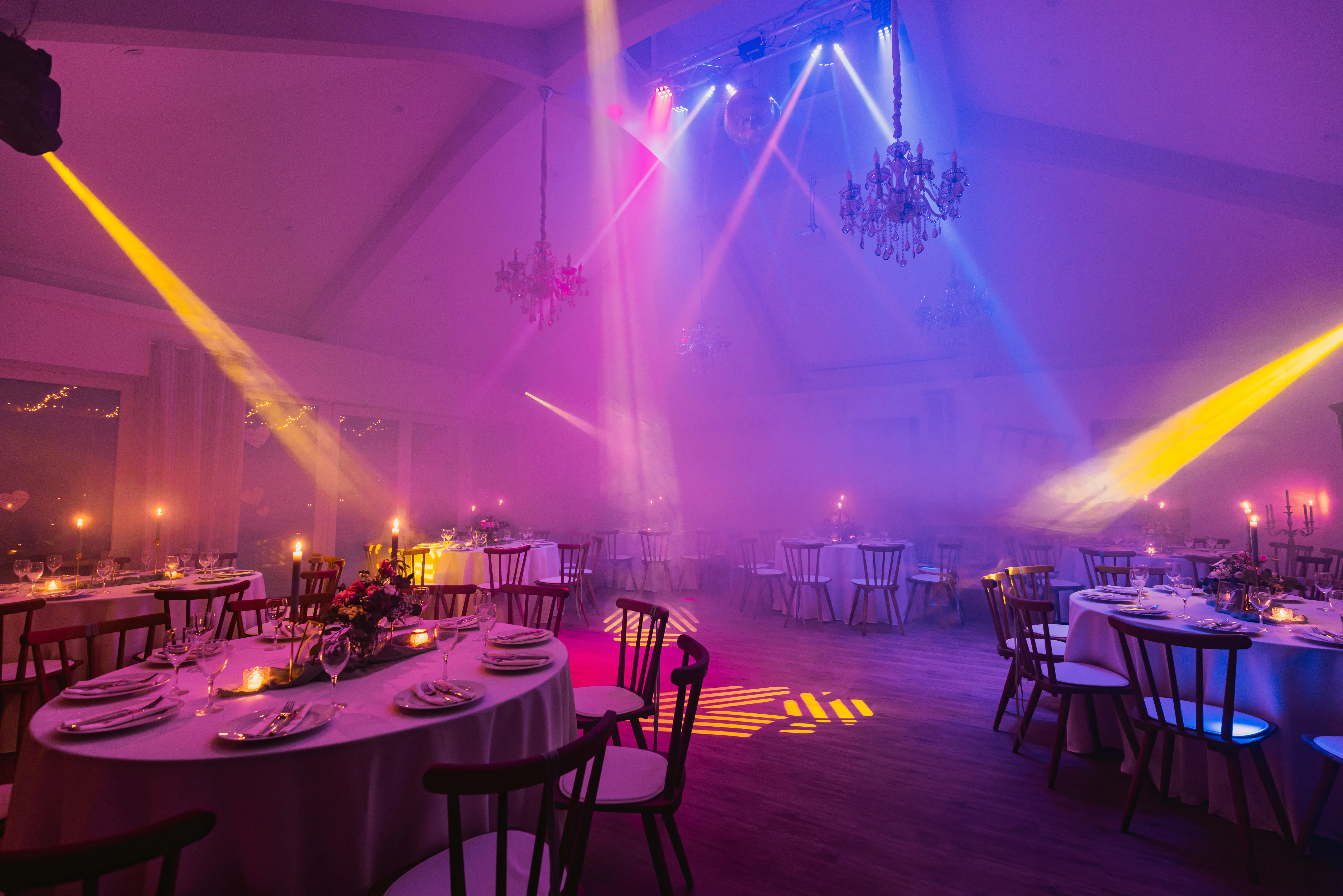 Festsaal bei Nacht mit gelben und blauen Lichtkegeln, Kronleuchtern und festlich gedeckten Tischen