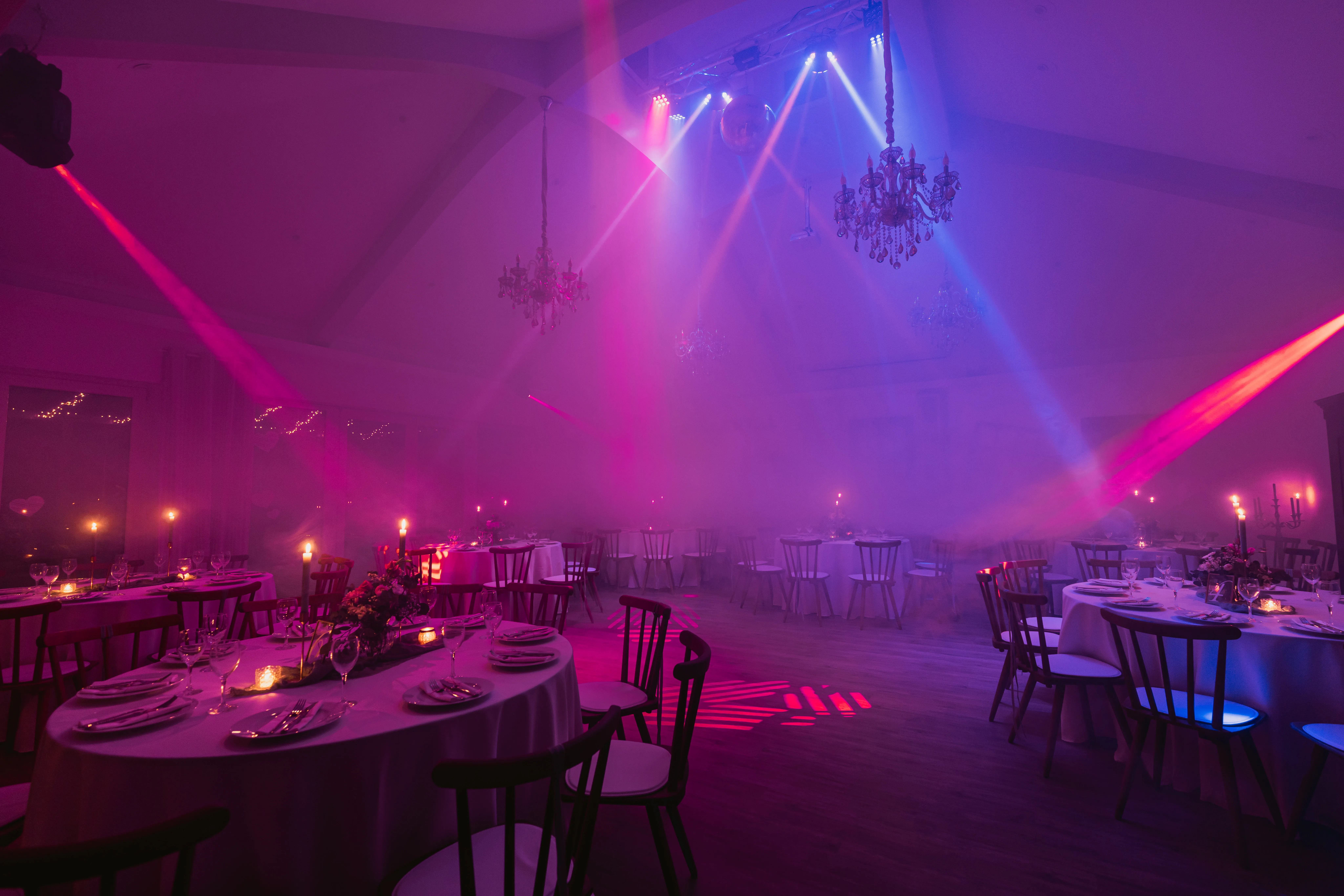 Festsaal in kräftigem Pink-Magenta-Licht mit Scheinwerferstrahlen, Nebel und gedeckten Tischen
