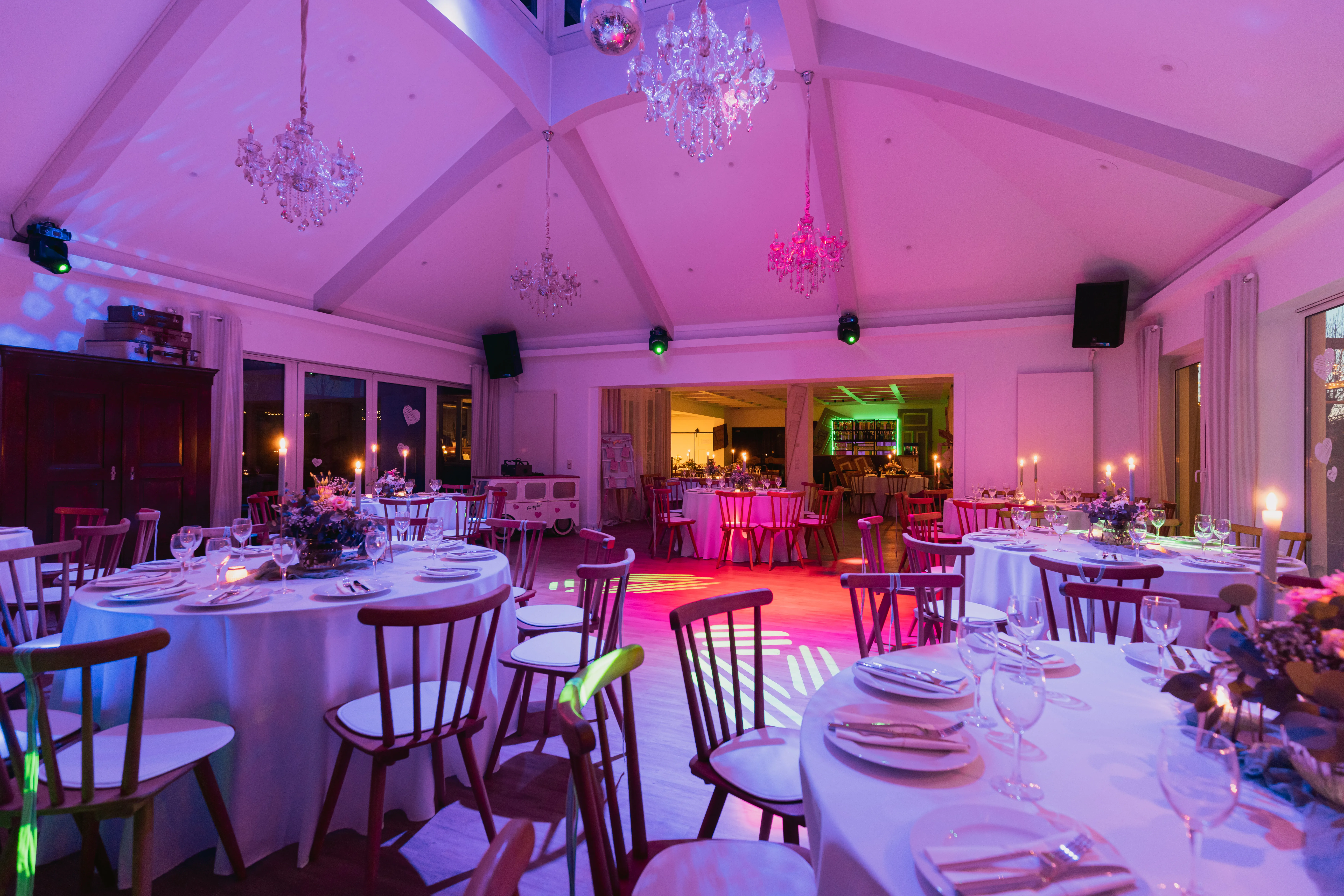 Festsaal in pinkem Partylicht mit Blick zum beleuchteten Barbereich und Candy-Bar-Wagen