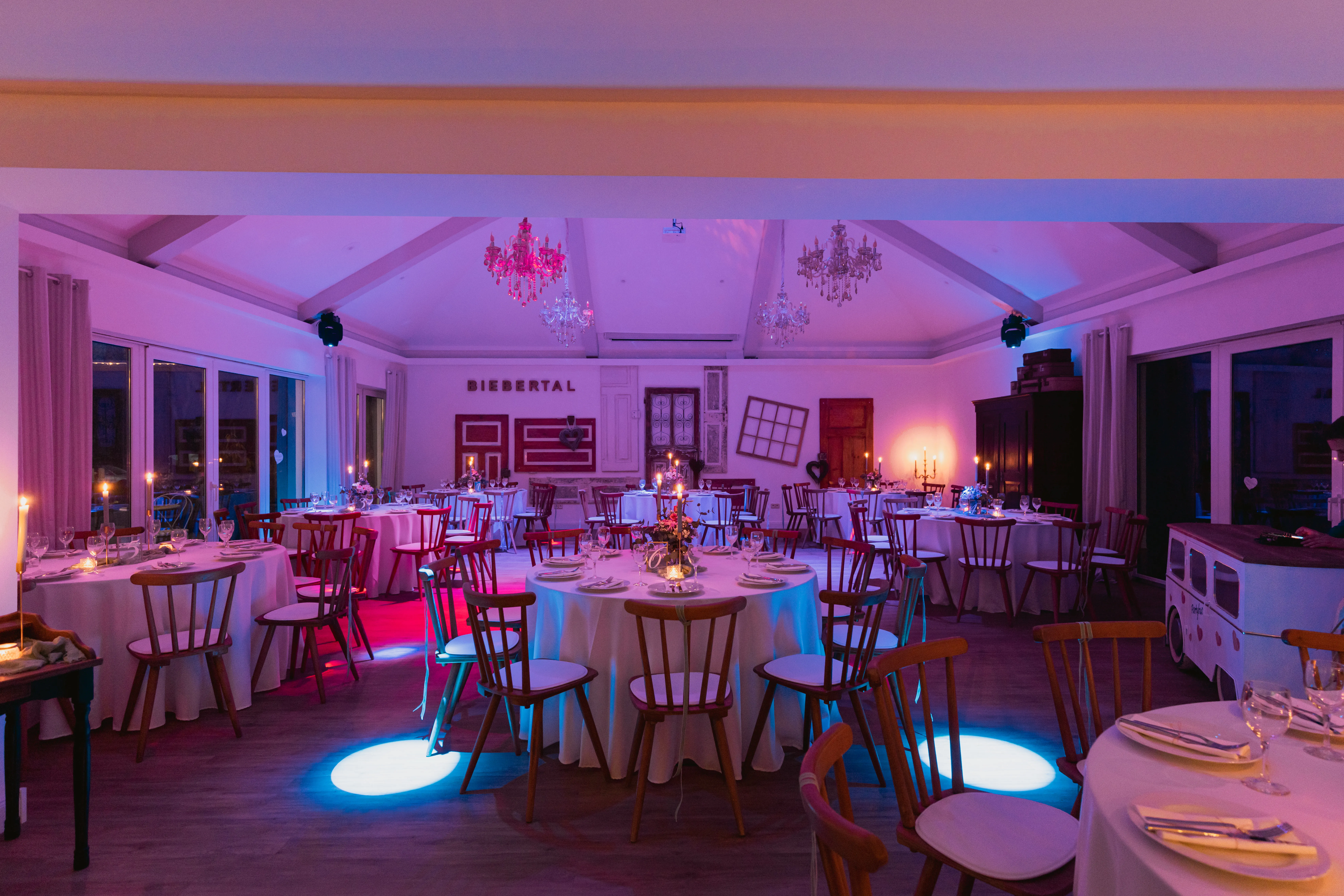 Festsaal bei Nacht in rosa-blauem Eventlicht mit angestrahlten Kronleuchtern und gedeckten runden Tischen