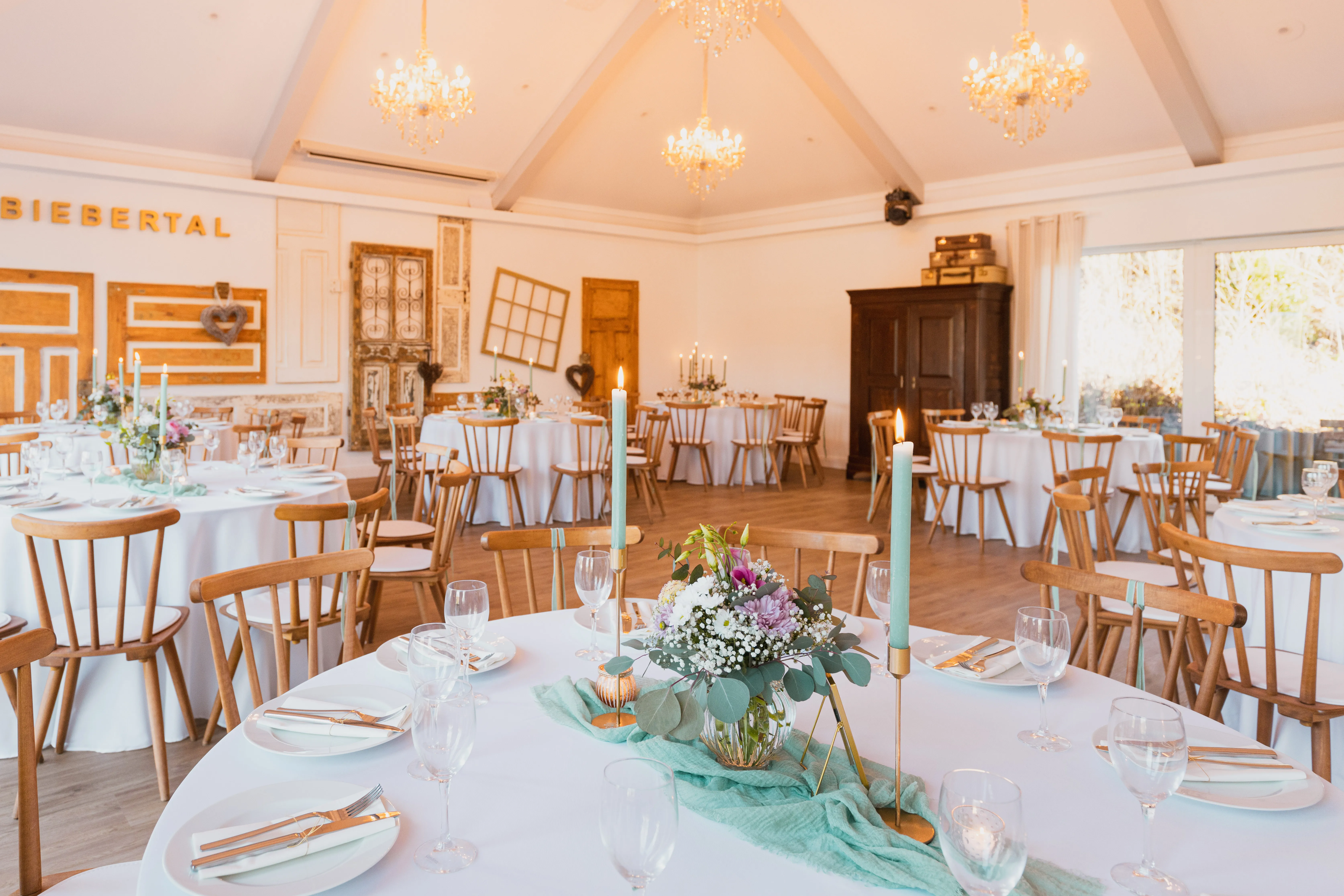 Festsaal mit antiker Türenwand, Kronleuchtern und Tafel mit mintgrüner Kerzendeko