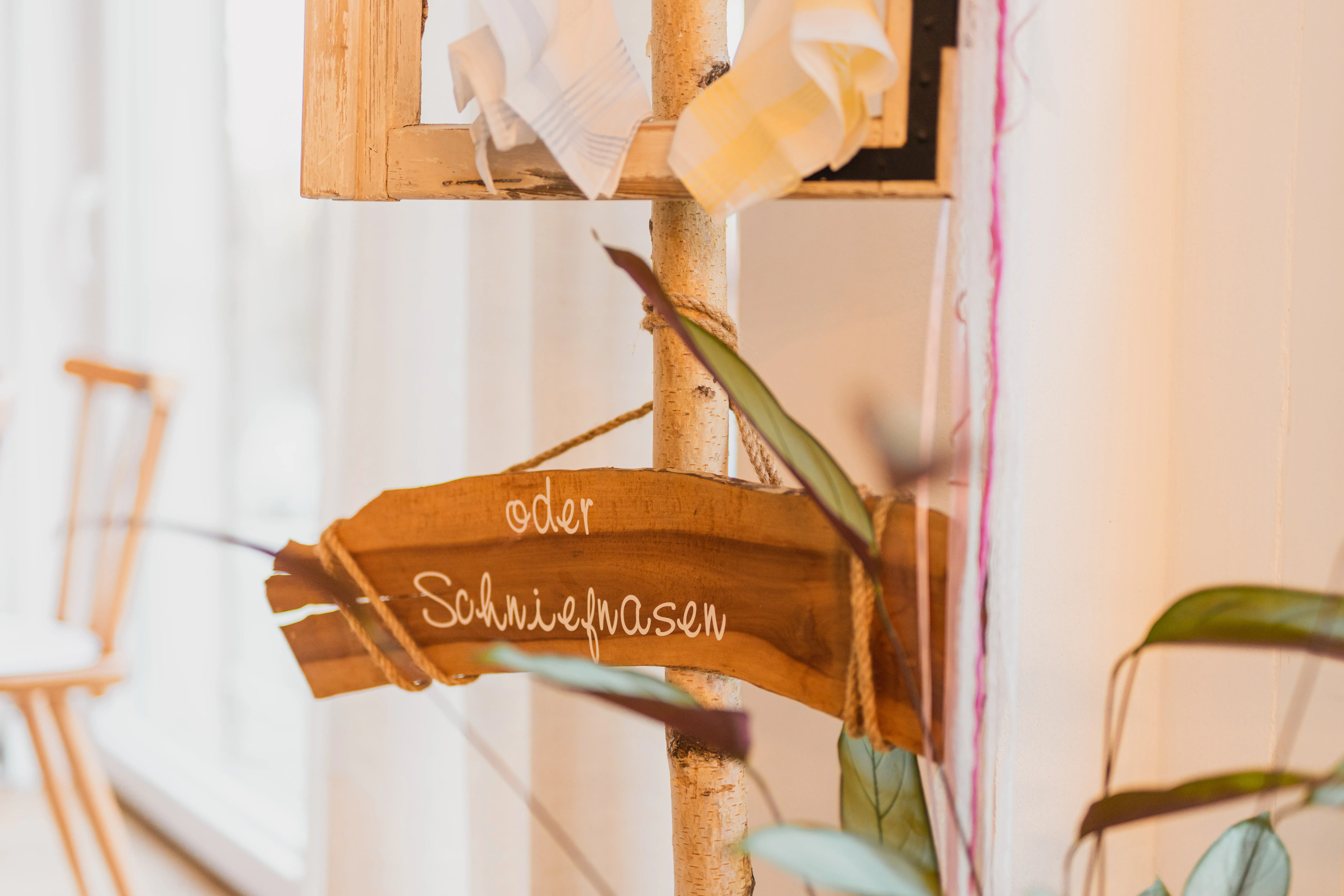 Holzschild 'oder Schniefnasen' mit Stofftaschentüchern an einem Birkenstamm, humorvolle Hochzeitsdeko