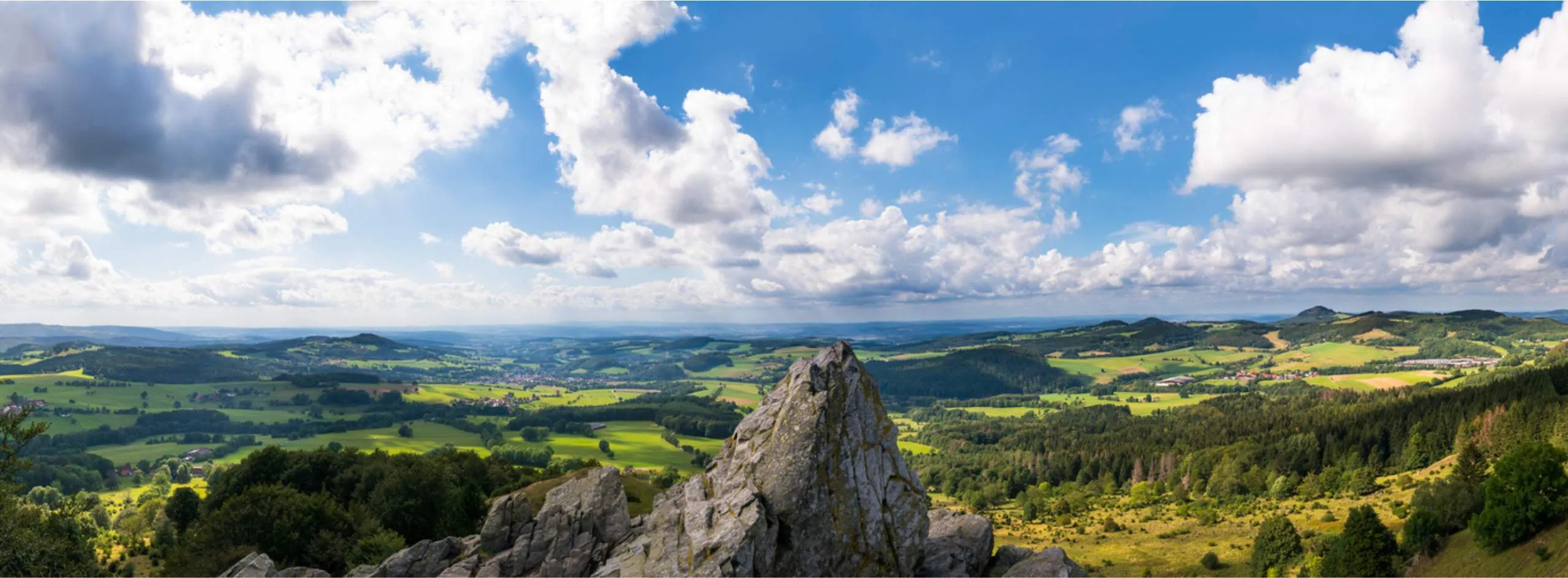 Panoramablick über die grüne Rhön-Landschaft mit Felsen im Vordergrund und Wolkenhimmel