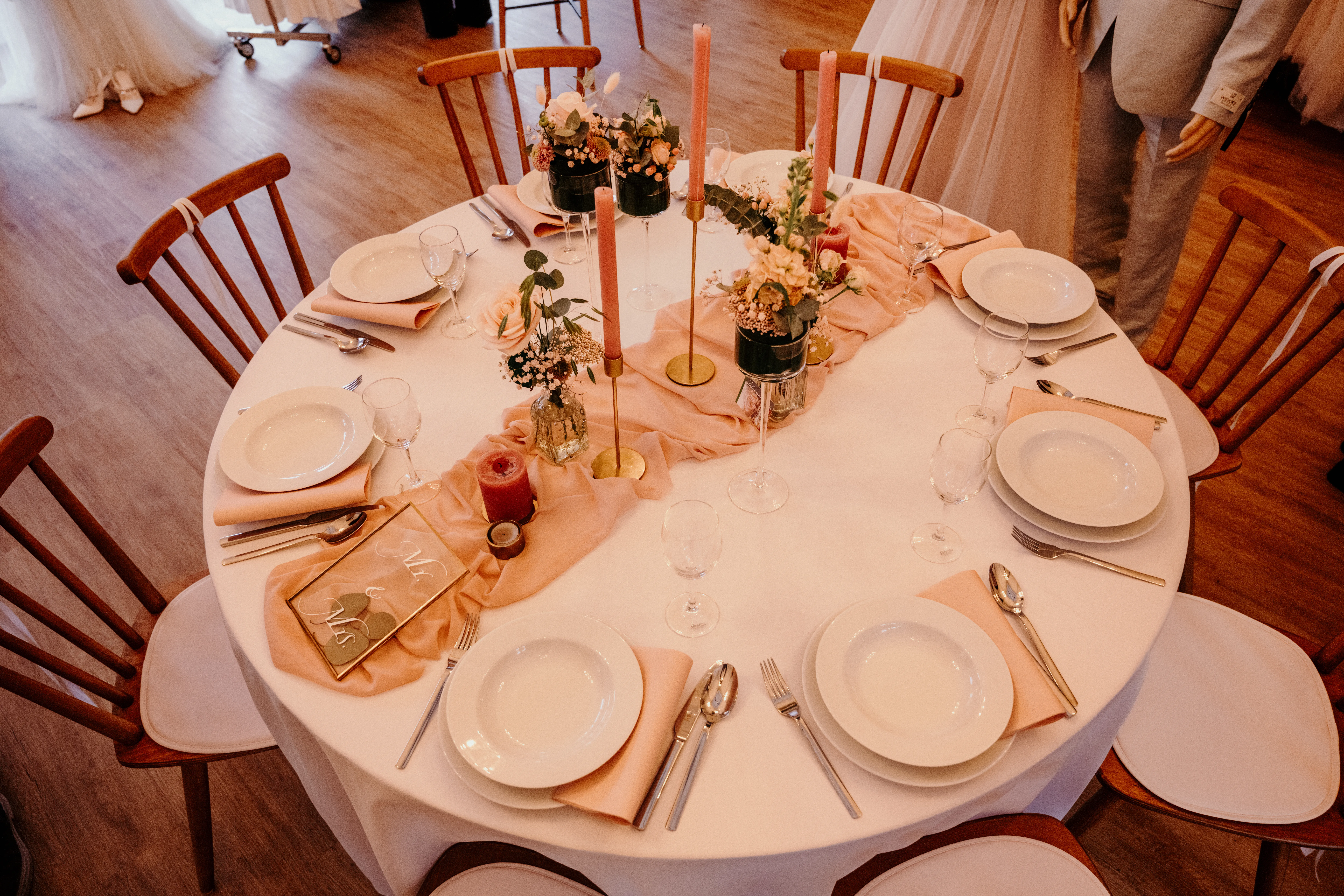 Rund eingedeckte Hochzeitstafel mit apricotfarbener Deko, rosé Kerzen und Blumen von oben