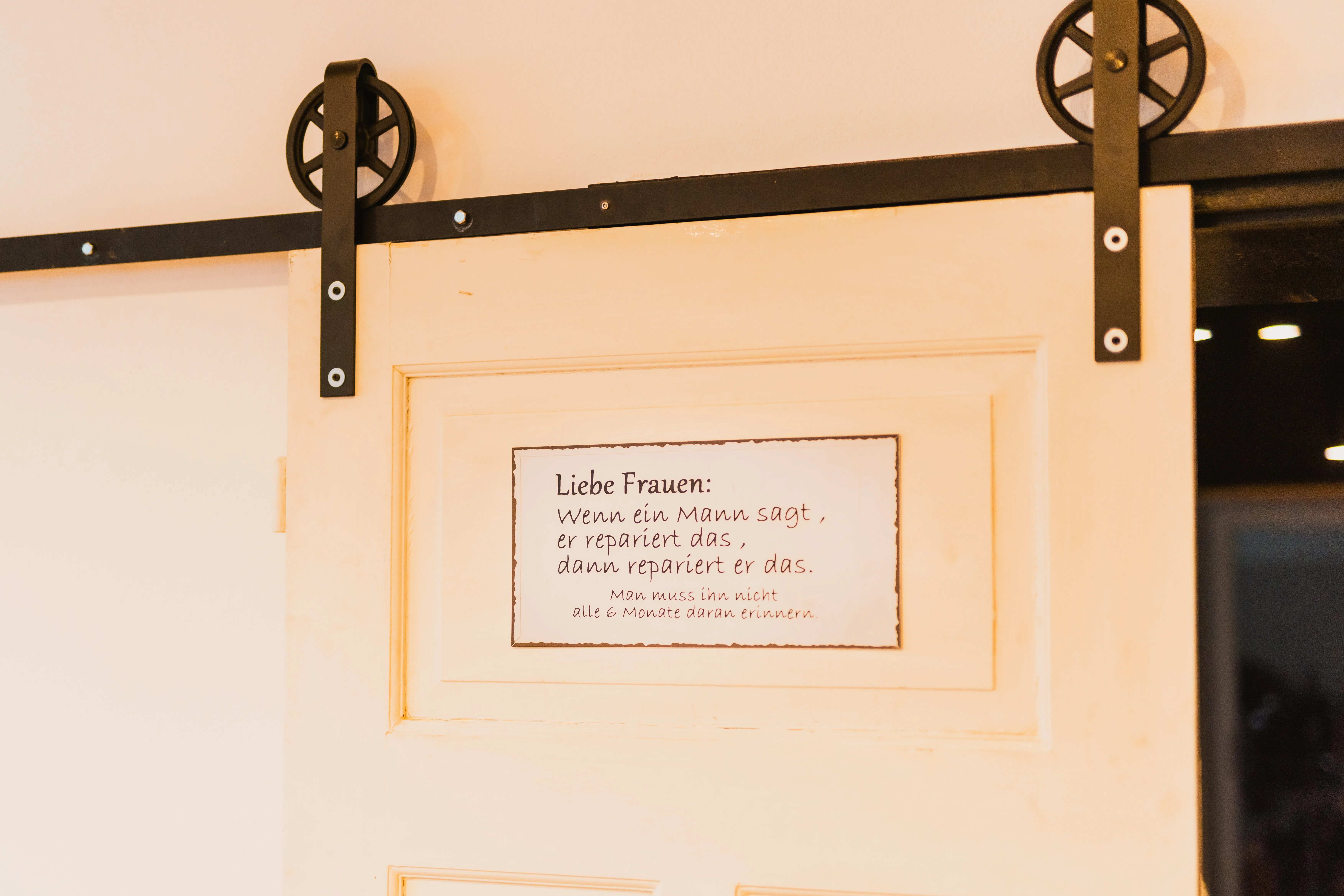 Cremefarbene Vintage-Schiebetür mit Laufrollen und Spruchschild