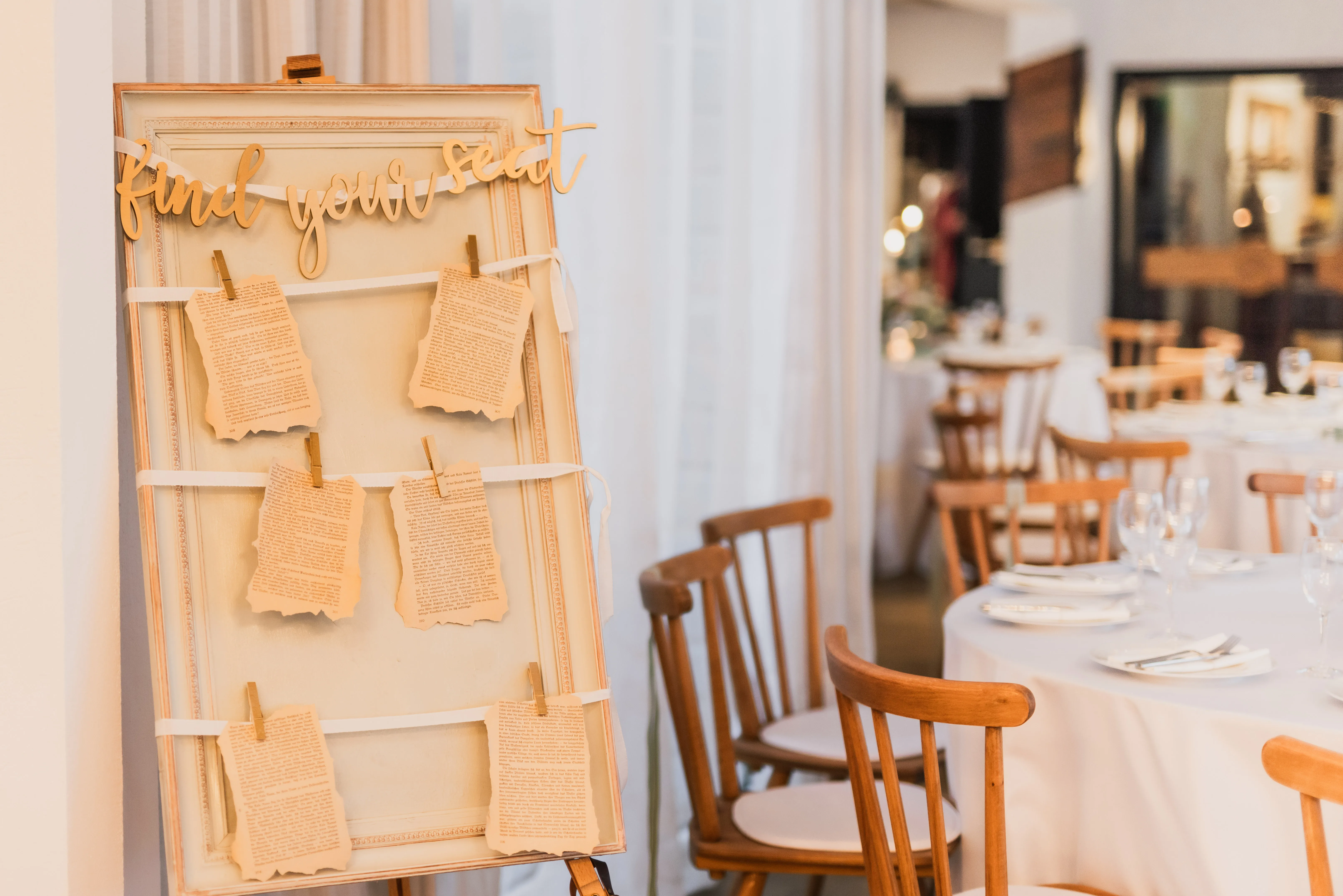 Sitzplan 'find your seat' auf Vintage-Staffelei, dahinter gedeckte runde Tische mit Holzstühlen
