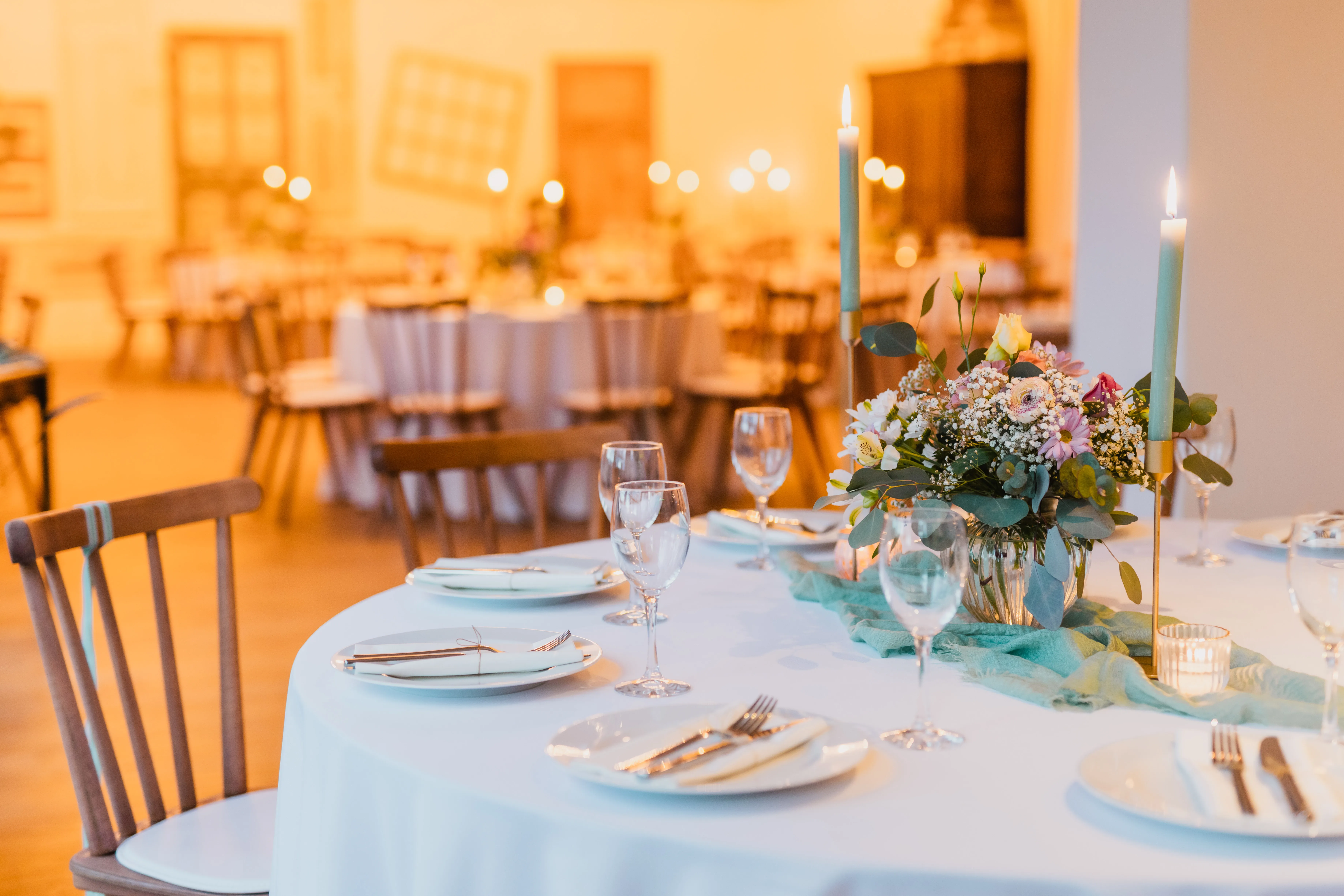 Runder Tisch mit Pastellblumen, goldenen Kerzenhaltern und grünen Kerzen im Festsaal